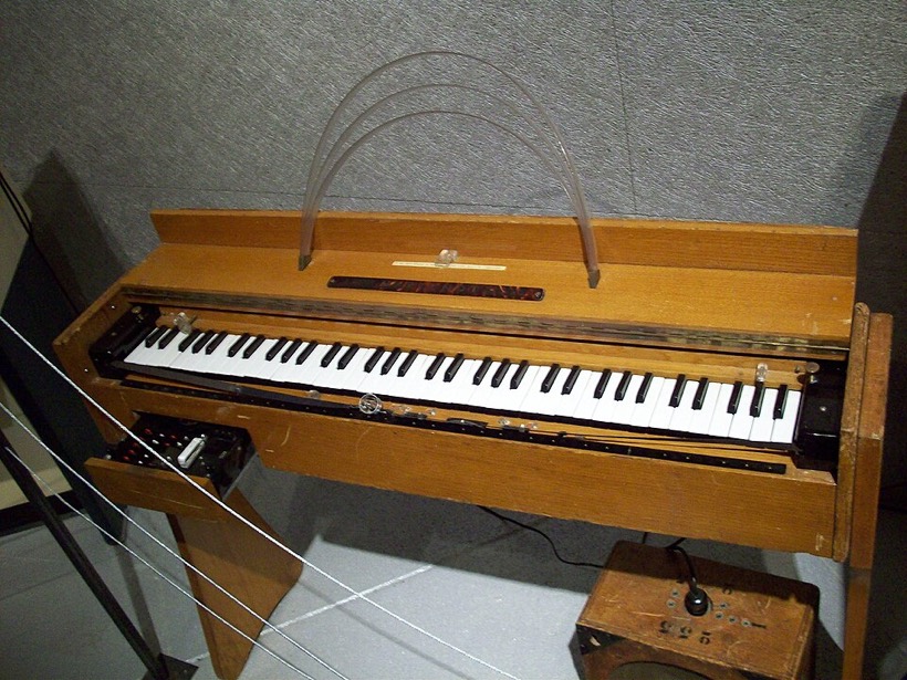Fotografia: drewniany instrument z klawiaturą i łukami nad nią, obok mały głośnik